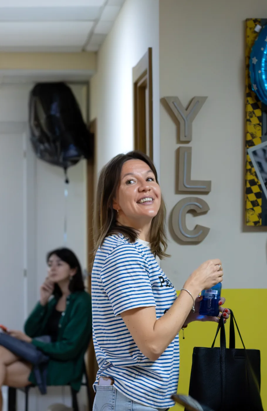 Студентка улыбается у букв YLC на стене школы