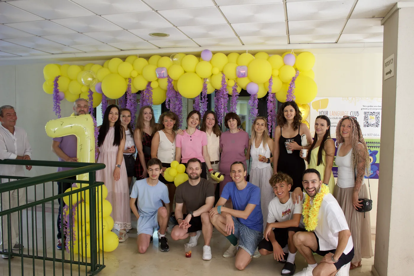 Students and teachers celebrating the anniversary under yellow and purple balloons
