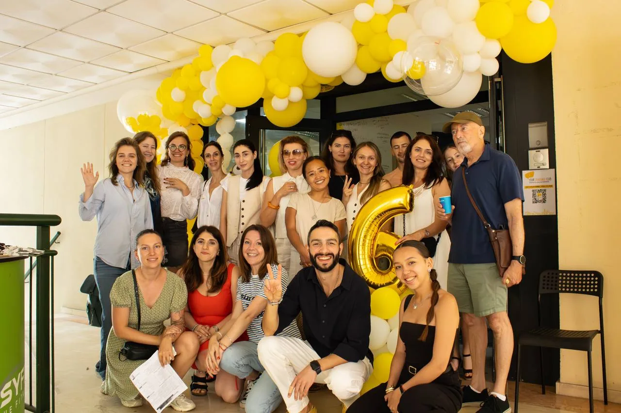 Students and teachers posing under the anniversary balloon arch