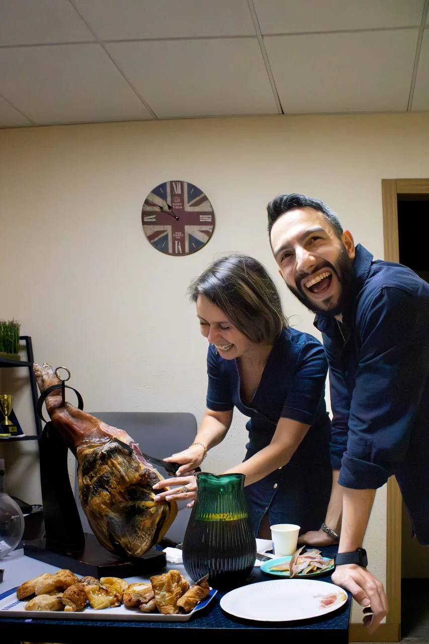A teacher and a student carving jamón together and laughing
